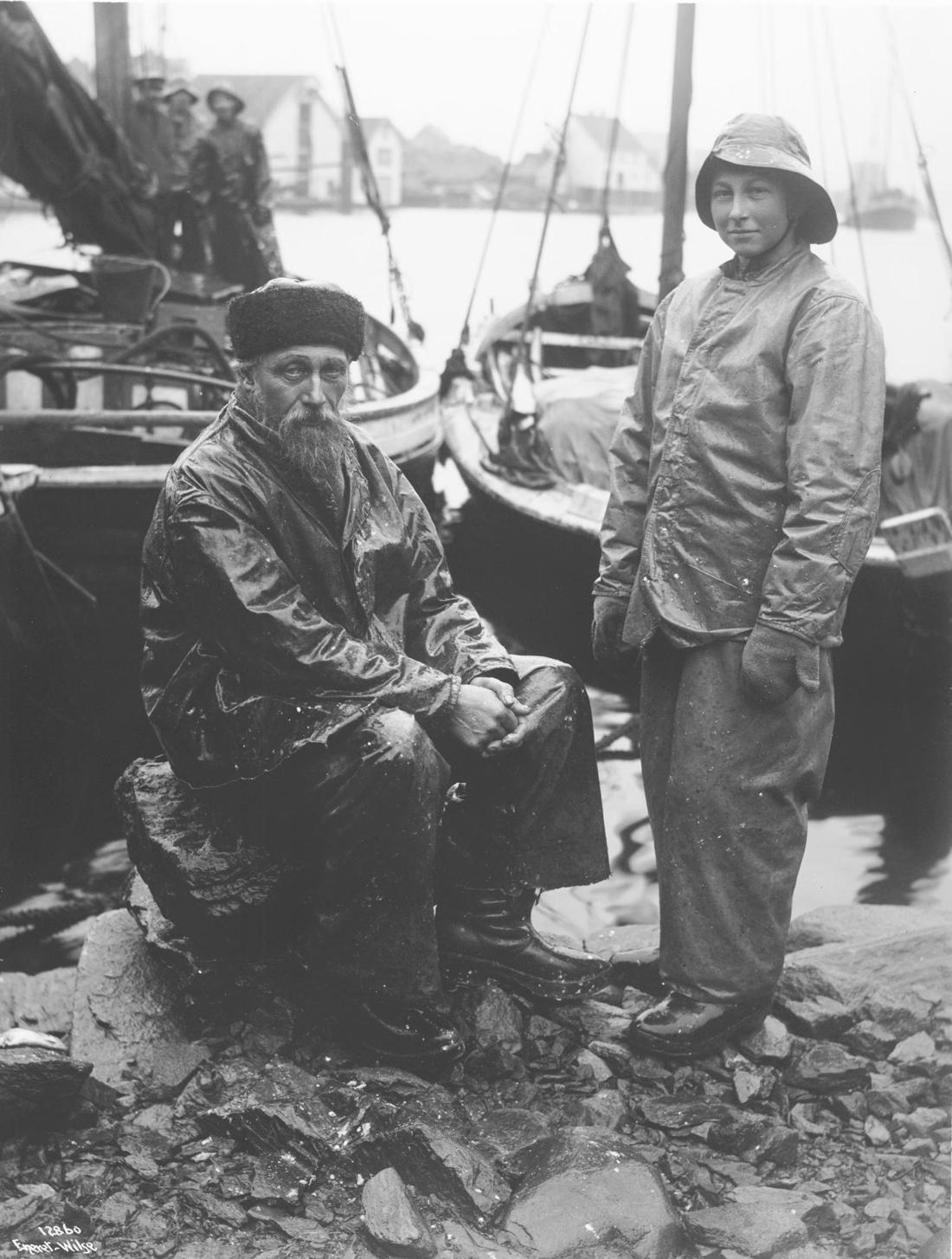 Gammel fisker med skjegg og sønnen hans i oljehyre på berget i Kopervik, 1911